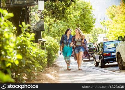 Two female friends strolling on roadside arm in arm, Franschhoek, South Africa