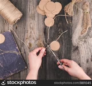two female hands and paper tags with a brown rope on a gray wooden table, top view