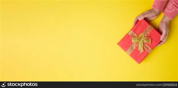 two female hands are holding red gift box on a yellow background, concept of congratulations on birthday, copy space