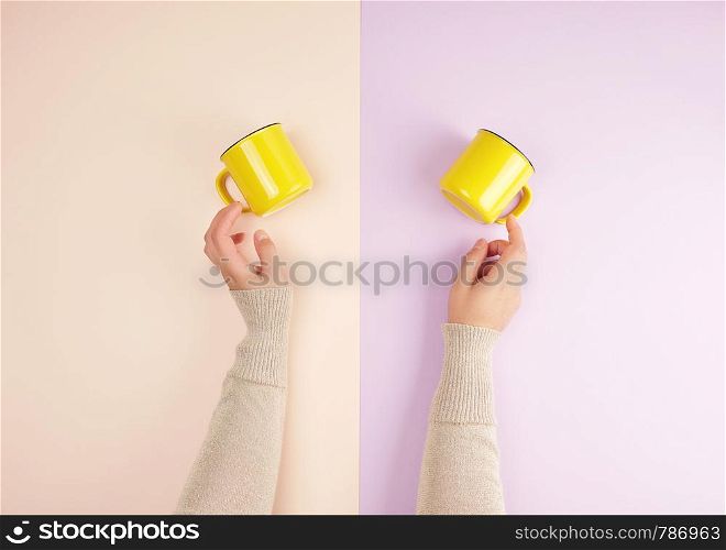 two female hands are holding yellow ceramic cups on a colored background, top view