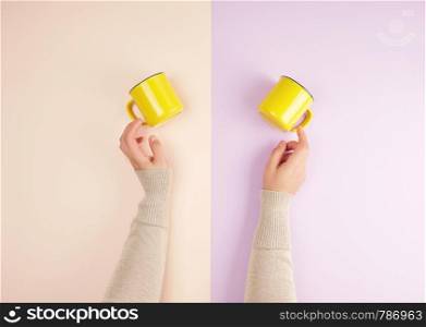 two female hands are holding yellow ceramic cups on a colored background, top view