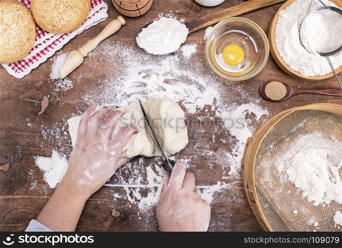two female hands cut with a knife yeast dough into pieces for making buns, top view