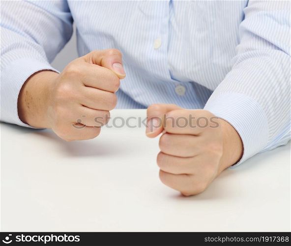 two female hands folded into a fist on a white table. Strict leader, aggression and pressure on the person