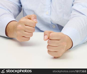 two female hands folded into a fist on a white table. Strict leader, aggression and pressure on the person