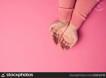 two female hands folded palm to palm on a pink background, top view