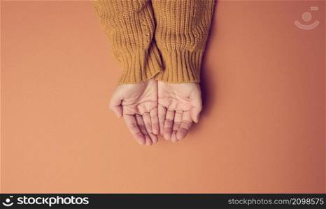 two female hands folded palm to palm on an orange background, top view