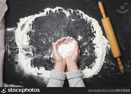two female hands hold a handful of white wheat flour on a black table, top view