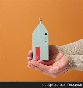 two female hands hold a miniature wooden house on a brown background. Real estate insurance concept, environmental protection, family happiness
