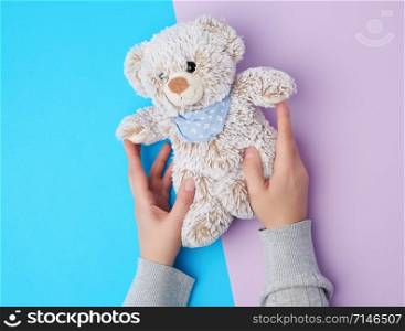 two female hands hold a small toy teddy bear on a blue background, top view