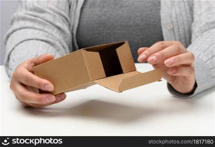 two female hands hold a square box made of brown corrugated cardboard on a white background, close up