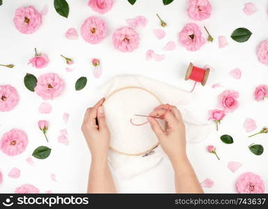 two female hands holding a round wooden hoop and a red thread with a needle, the concept of embroidery products, top view