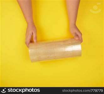 two female hands holding a stack of transparent scotch on a yellow background, adhesive tape