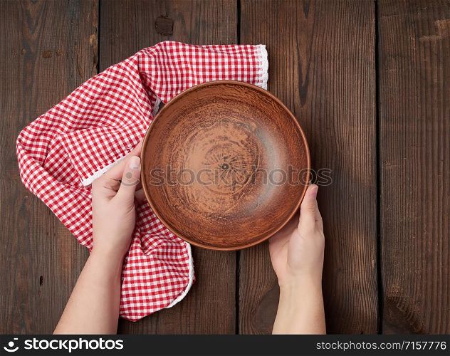 two female hands holding an empty round clay plate, top view
