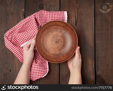 two female hands holding an empty round clay plate, top view