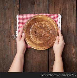 two female hands holding an empty round wooden plate, top view