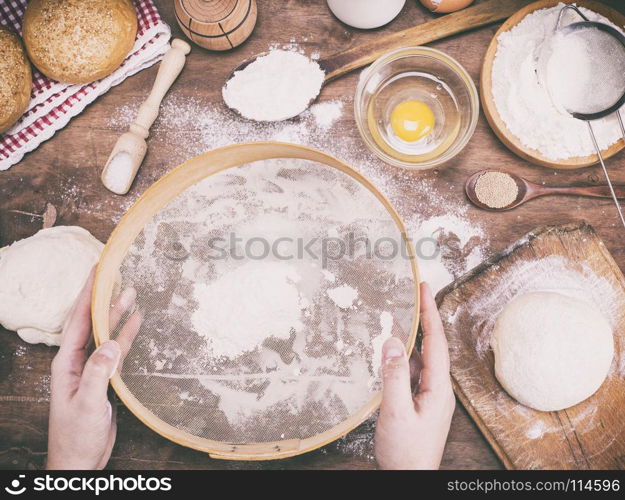 two female hands holding an old wooden sieve for flour above the kitchen table, vintage tonin