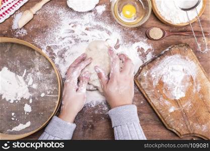 two female hands interfere with a ball of yeast dough on a brown woody background, the top view