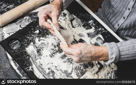 two female hands knead the dough from white wheat flour on a black table, top view