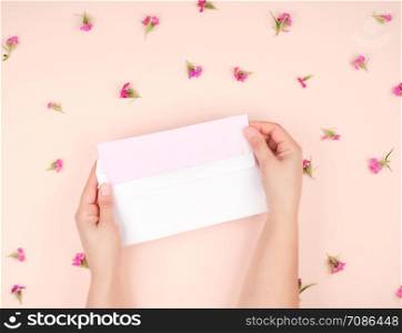 two female hands open white paper envelope, in the middle a letter on pink paper, top view, concept of receiving and sending correspondence