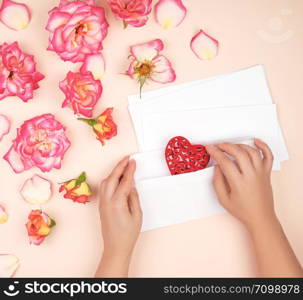 two female hands put a red heart in a white paper envelope, concept of congratulations on the holiday and love