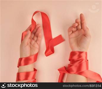 two female hands wrapped in a red satin ribbon, peach background, top view
