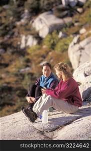 Two Female Hikers Sitting On A Rock And Resting Together