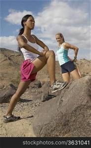 Two female joggers stretching in mountains