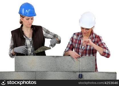 Two female mason working on a wall.