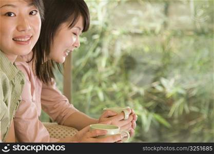 Two female office workers holding coffee cups and smiling