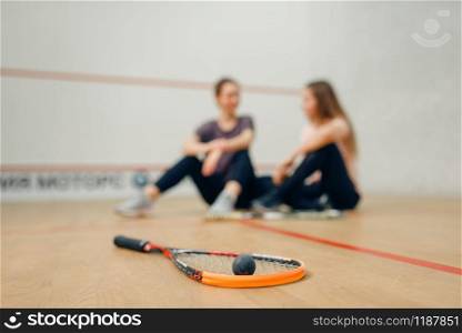 Two female players with squash rackets sits on court floor. Girls on training, active sport hobby, fitness workout for healthy lifestyle. Two players with squash rackets sits on floor
