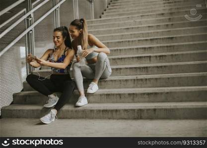 Two female runners looking on smart phone an rest after jogging in urban envionment