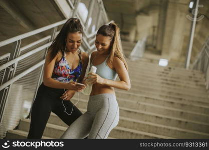 Two female runners looking on smart phone an rest after jogging in urban envionment