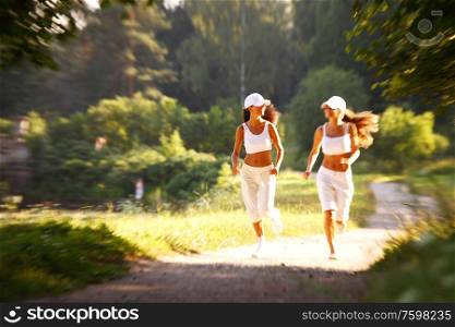 Two female runners run in summer park, women friends. Two women run in park