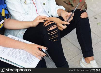 Two female students are preparing for exams with workbook and tablet PC in urban background. Education concept.