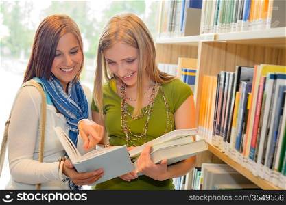Two female students at school library standing and reading book