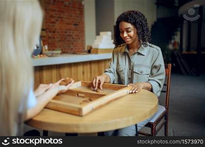 Two female students play board game in cafe. Women leisures in coffeehouse, education and food. Girls studying in campus cafeteria. Two female students play board game in cafe