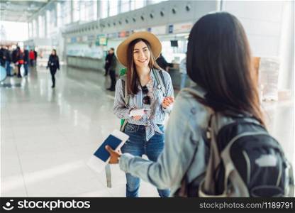 Two female tourists with bags waiting for departure in international airport. Passengers with baggage in air terminal, back view, happy journey of white and black ladies, summer travel of happy women