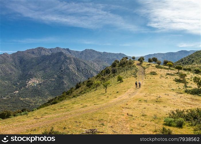 Two female walkers on a track near Novella in the Balagne region of north Corsica with the village of Lama and mountains in the background