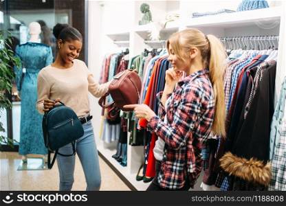 Two females choosing bags in shop, shopping. Shopaholics in clothing store, consumerism lifestyle, fashion. Two females choosing bags in shop, shopping
