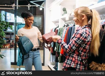 Two females choosing bags in shop, shopping. Shopaholics in clothing store, consumerism lifestyle, fashion