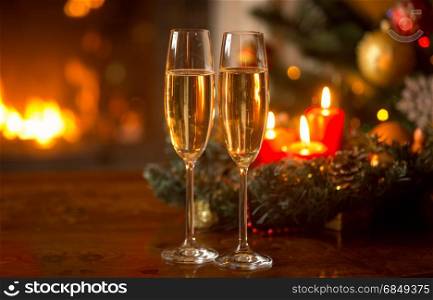 Two filled champagne glasses in front of Christmas wreath with burning candles