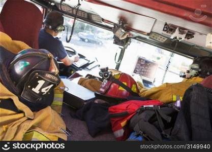 Two firefighters driving a fire engine with gear in the back (selective focus)