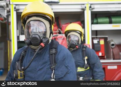 Two firemen in masks standing near fire engine (depth of field)