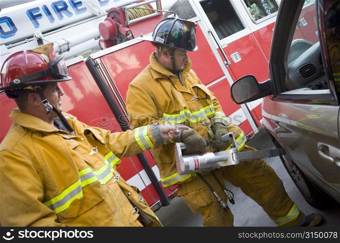 Two firemen using the jaws of life on a car door