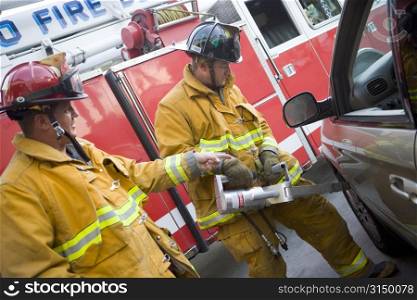 Two firemen using the jaws of life on a car door