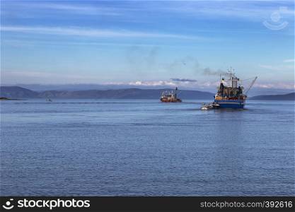 two fishing trawlers leave the port in early evening
