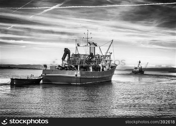 two fishing trawlers leave the port in early evening, black and white classic photo