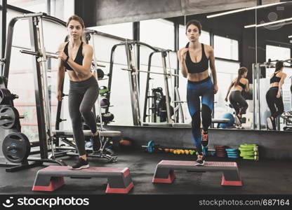 Two fit attractive women doing workout with steppers in the gym