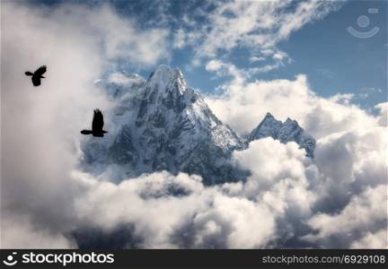 Two flying birds against majestical Manaslu mountain with snowy peak in clouds in sunny bright day in Nepal. Landscape with beautiful high rocks and blue cloudy sky. Nature background. Fairy scene