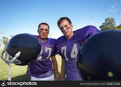 Two Football Players Holding Helmets